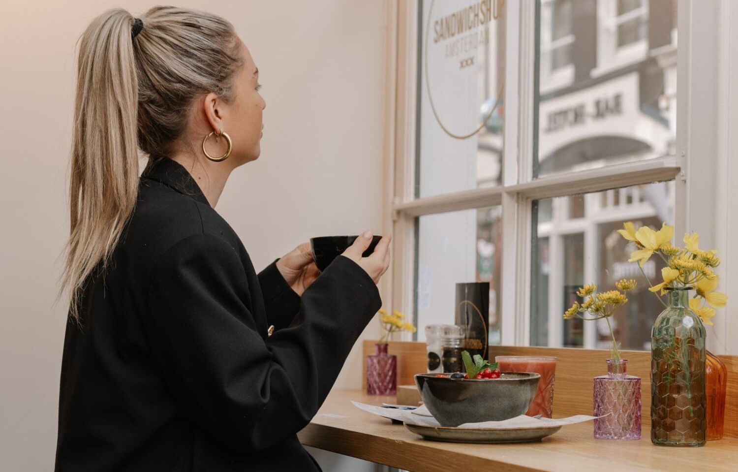 Alt: klant geniet van een versbereid ontbijt en koffie met uitzicht op de levendige Warmoesstraat