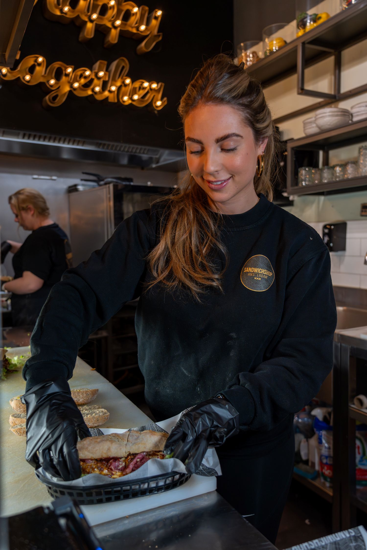 Alt: Een medewerkster van de Sandwichshop Amsterdam die met een glimlach een sandwich vers bereidt